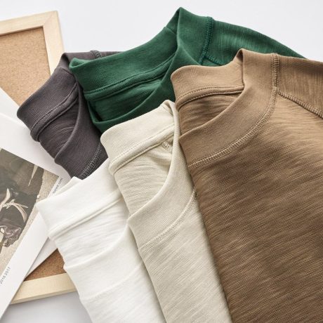 various colored crew neck t-shirts stacked on top of each other in neutral and earthy tones, including white, green, brown, and maroon.