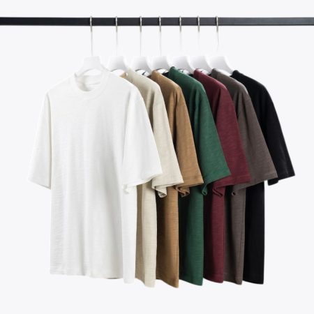 Multiple T-shirts in various colors neatly displayed, showing the comfortable fit and diverse color options of the 100% cotton fabric.