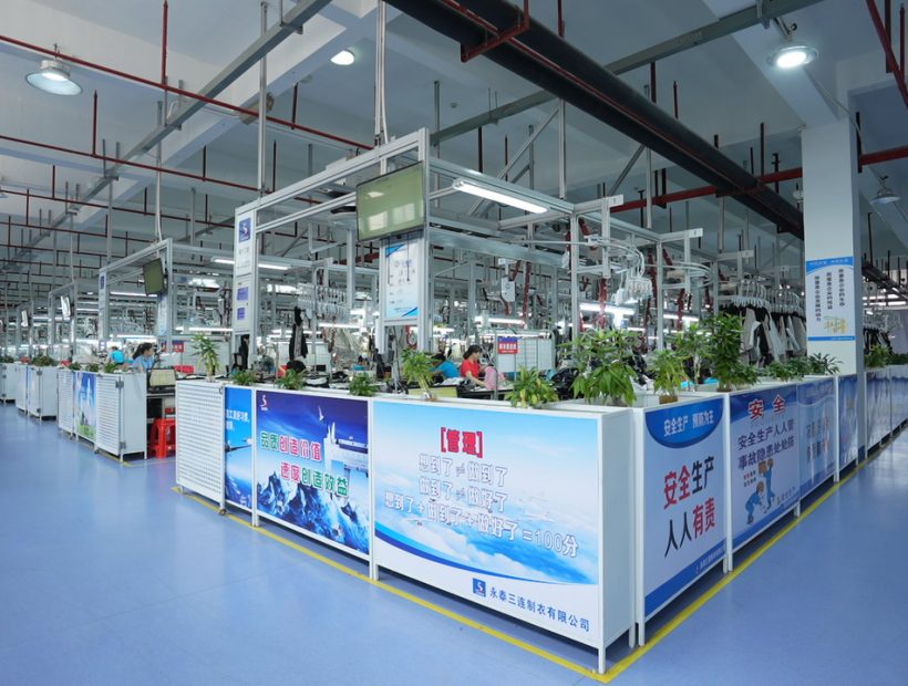Factory interior showing apparel production lines with workers and machinery.