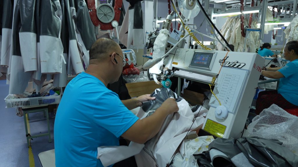 A detailed view of a technician operating an industrial seam-sealing machine to apply specialized tape to the interior seams of a waterproof jacket, ensuring maximum weather protection.