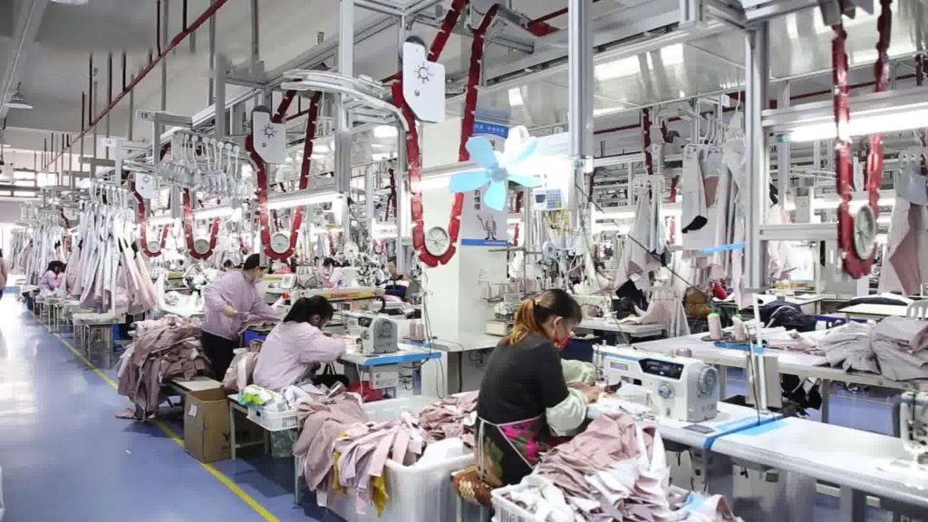 A view of a garment production line featuring numerous workers operating industrial sewing machines, highlighting the high-volume manufacturing process for technical outerwear.