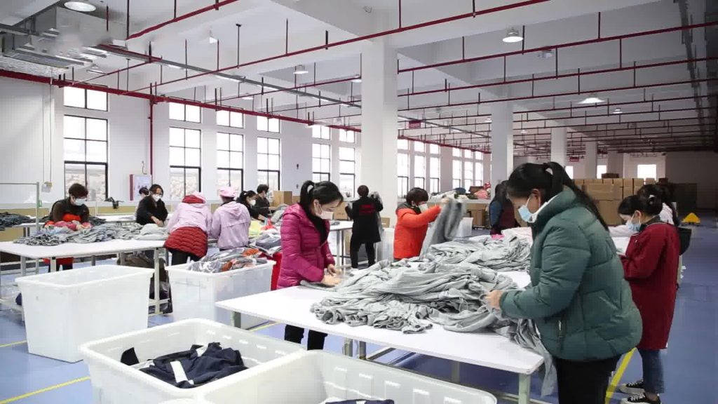 Workers sorting finished garments at inspection tables representing final quality control before apparel shipment