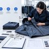 A professional quality control inspector conducting an AQL evaluation on a navy jacket in a garment factory. The scene illustrates the standard inspection workflow—from random sampling to defect classification—supported by on-site tools like measurement tapes, fabric swatches, and detailed inspection checklists to ensure product compliance.
