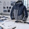 Overview of the apparel manufacturing process showing design tech packs, fabric swatches, hardware accessories, and a finished jacket on a worktable.